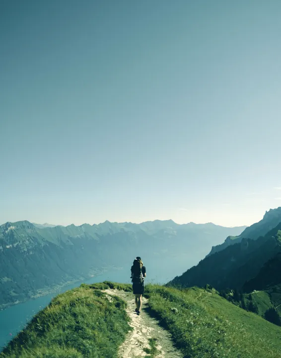A hiker walking along a grassy mountain ridge above a lake