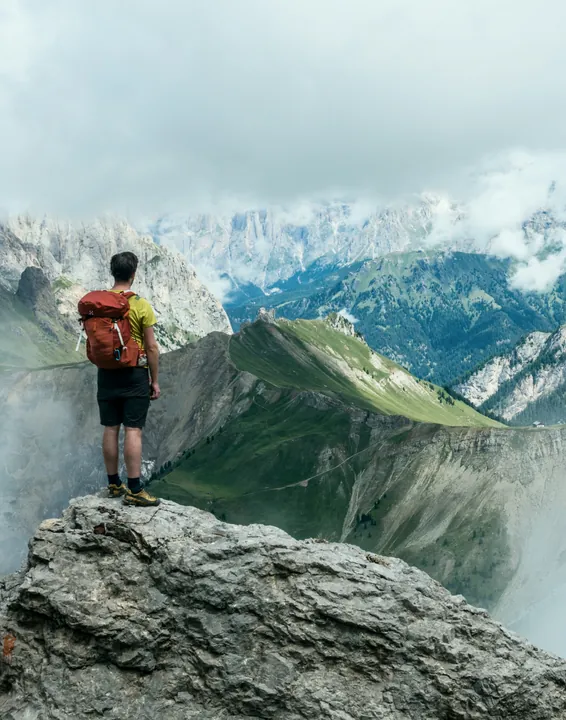A hiker with a backpack standing on a rocky peak above the clouds
