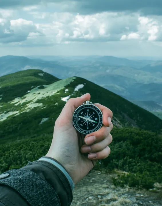 A hand holding a compass on a mountain trail
